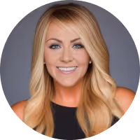 Smiling blonde woman with long hair wearing a black sleeveless top against a gray background.