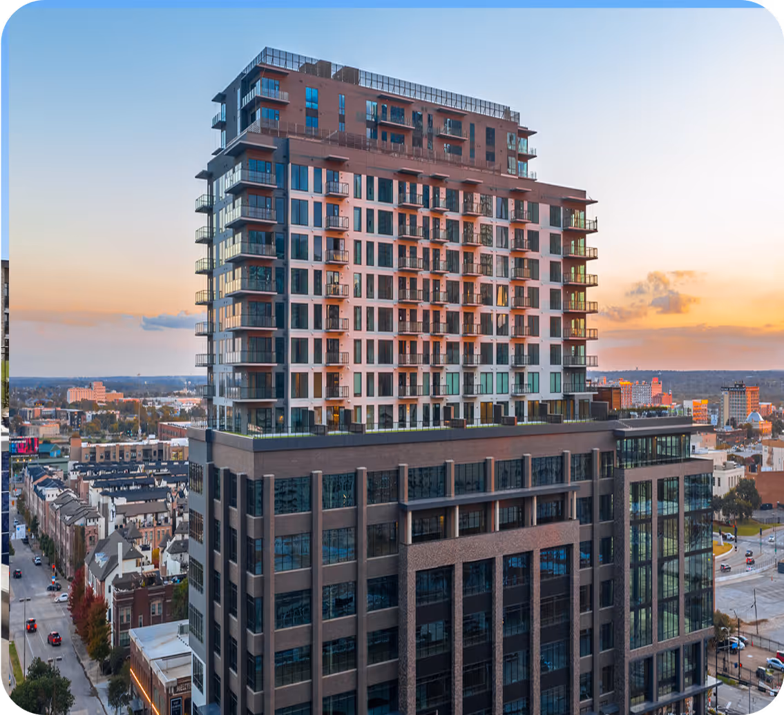 Modern high-rise building with glass balconies and a sunset sky over a cityscape.