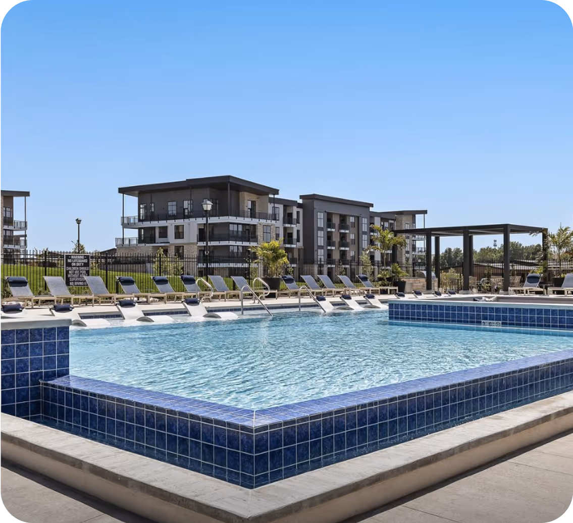 Modern apartment complex with an outdoor swimming pool surrounded by lounge chairs under clear blue sky.